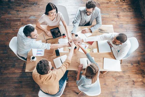 starting-new-working-day-as-a-team-top-view-of-group-of-six-young-people-holding-hands-together-and-smile-while-sitting-at-the-office-desk-photo